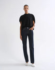A model stands against a plain white studio background wearing a black short-sleeve t-shirt, dark-wash straight-leg jeans, and white pointed shoes.