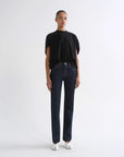 A model stands against a plain white studio background wearing a black short-sleeve t-shirt, dark blue straight-leg jeans, and white pointed shoes.