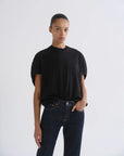 A model wearing a black short-sleeve crewneck t-shirt tucked into dark blue jeans, standing against a light gray studio background.