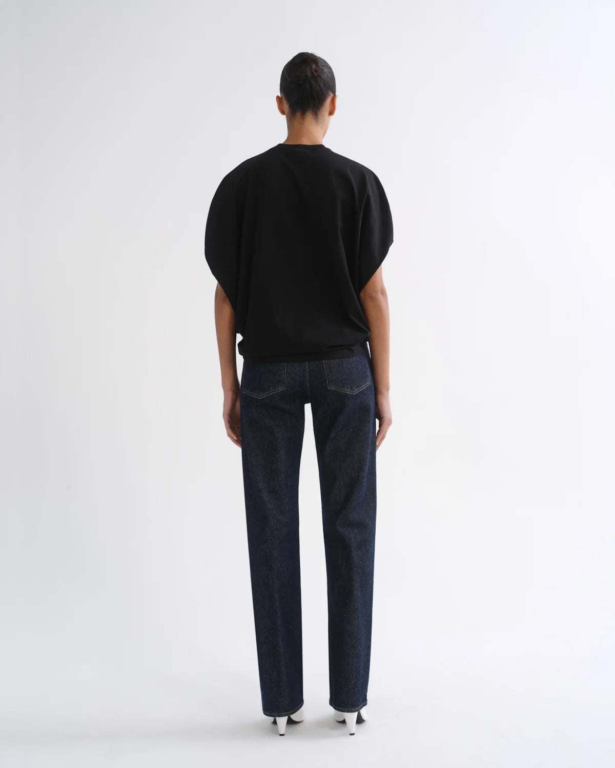 A model shown from the back wearing a black short-sleeve top and dark blue straight-leg jeans against a plain white studio background.