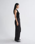 A woman in a black sleeveless top and black wide-leg cargo pants stands in profile against a light gray studio background.