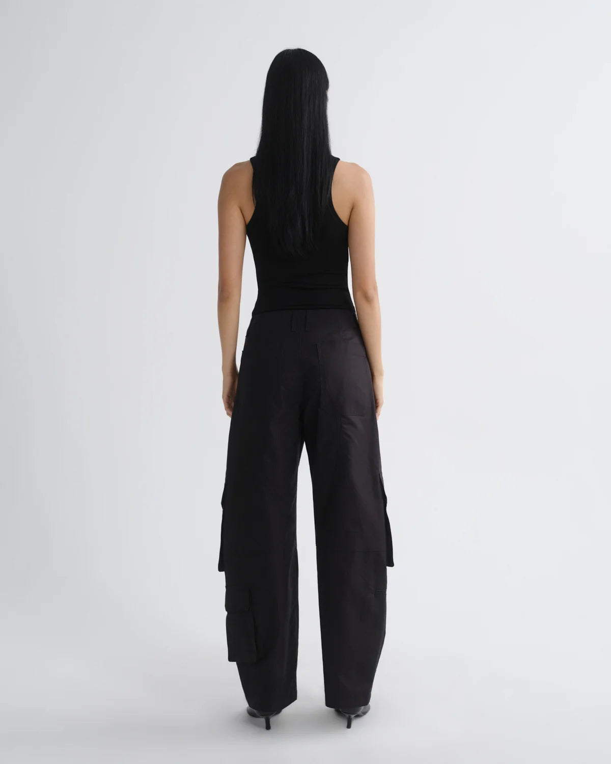 A model viewed from the back wearing a black sleeveless top and black wide-leg cargo pants against a light gray studio background.