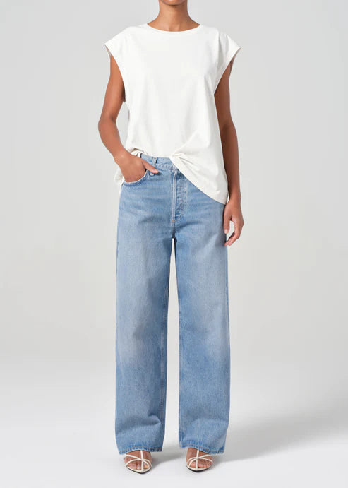 Person wearing a white sleeveless top and light blue jeans on a plain background front view
