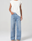 Person wearing a white sleeveless top and light blue jeans on a plain background front view