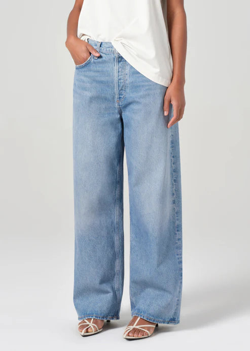 Person wearing light blue jeans and a white top on a plain background front view