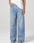 Person wearing light blue jeans and a white top on a plain background front view