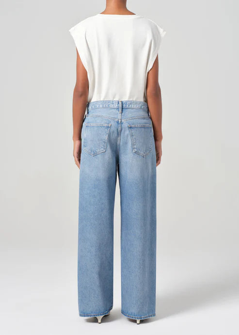 Person wearing light blue jeans and a white top on a plain background back view