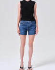 model wearing denim shorts with black shirt and heels on a white background 