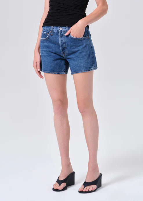 model wearing denim shorts with black shirt and heels on a white background 