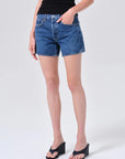 model wearing denim shorts with black shirt and heels on a white background 
