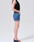 model wearing denim shorts with black shirt and heels on a white background, side view