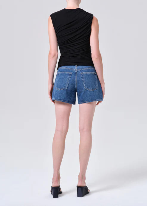 model wearing denim shorts with black shirt and heels on a white background, back view