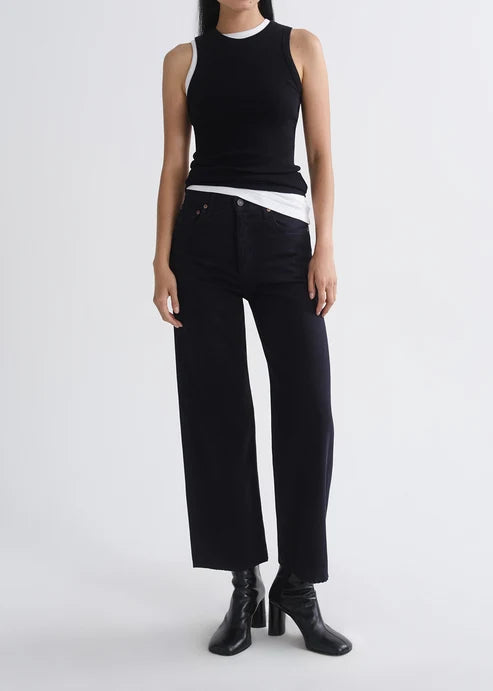 A model wearing a black sleeveless ribbed top with white shoulder panels, black wide-leg cropped pants, and black heeled ankle boots, photographed against a light gray studio background.