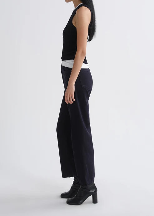 A model shown from the side wearing a black sleeveless top, wide-leg navy trousers, and black ankle boots against a plain light gray studio background.