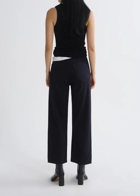 A model shown from the back wearing black wide-leg cropped trousers, a black sleeveless top, and black boots against a plain light gray studio background.