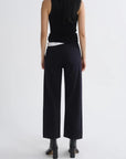 A model shown from the back wearing black wide-leg cropped trousers, a black sleeveless top, and black boots against a plain light gray studio background.