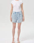 model wearing light wash denim shorts with a white top on a white background 