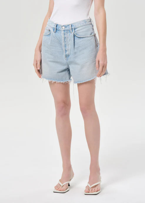 model wearing light wash denim shorts with a white top on a white background 