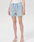 model wearing light wash denim shorts with a white top on a white background 