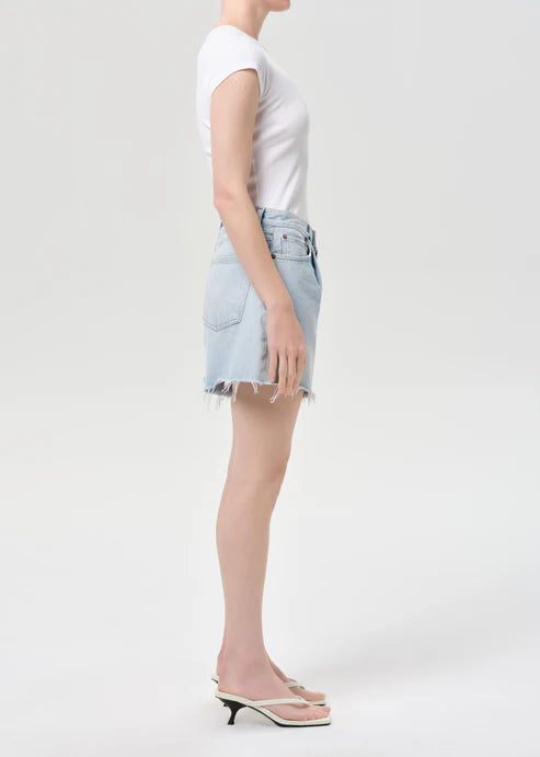 model wearing light wash denim shorts with a white top on a white background, side view