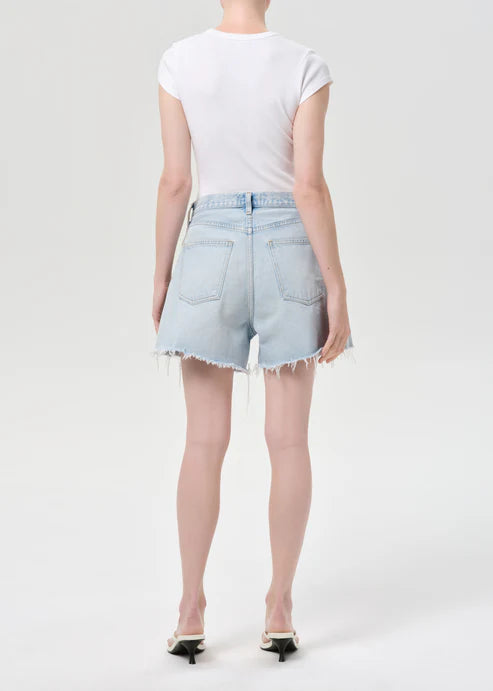 model wearing light wash denim shorts with a white top on a white background, back view
