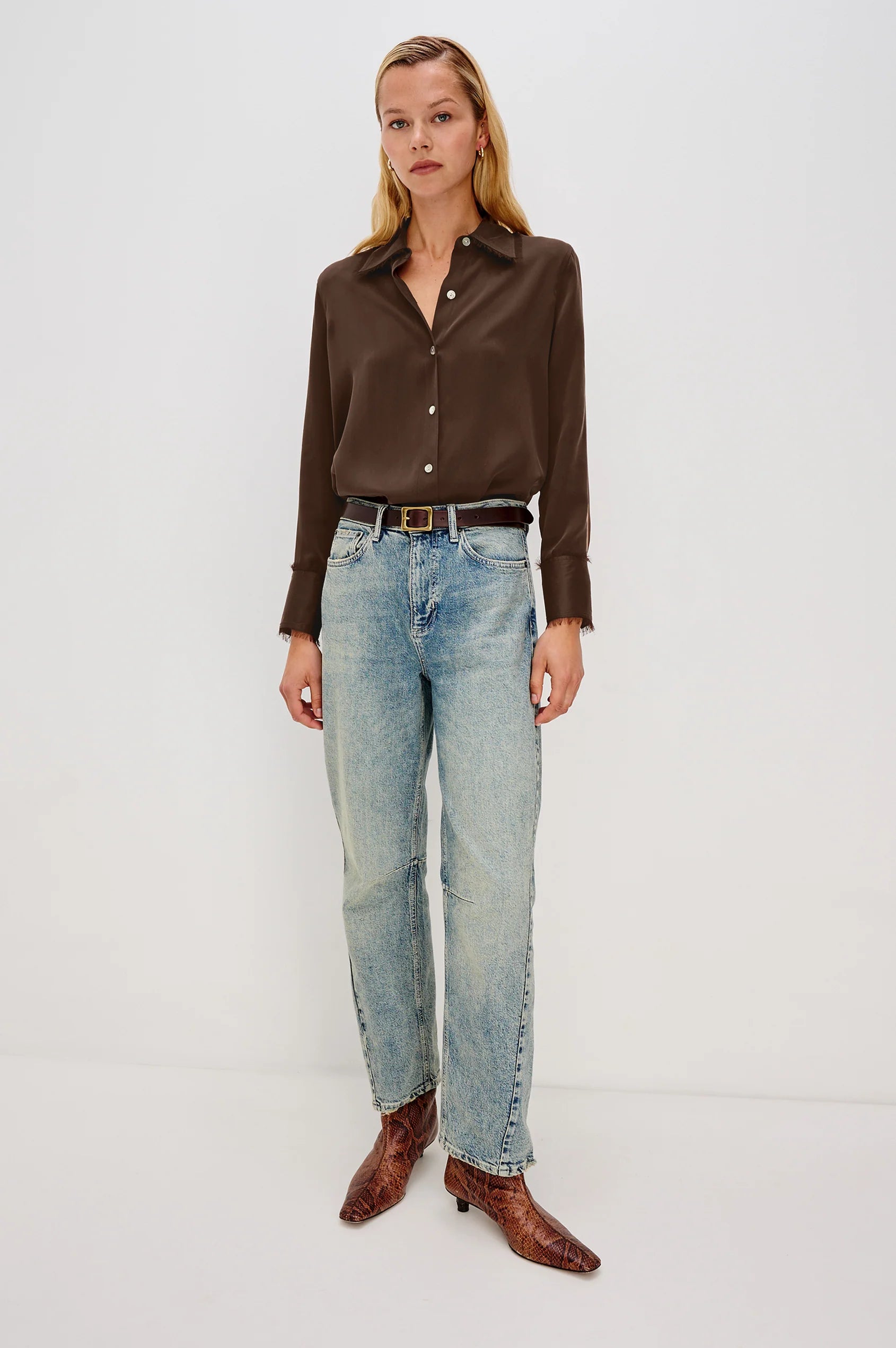Woman wearing a brown shirt, light blue jeans, and brown shoes on a white background