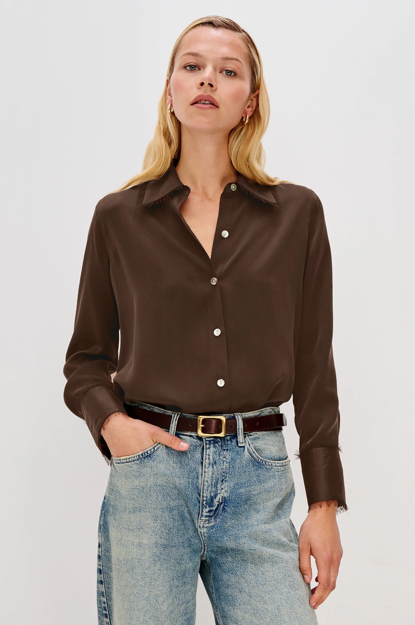 Woman wearing a brown button-up shirt and blue jeans on a white background