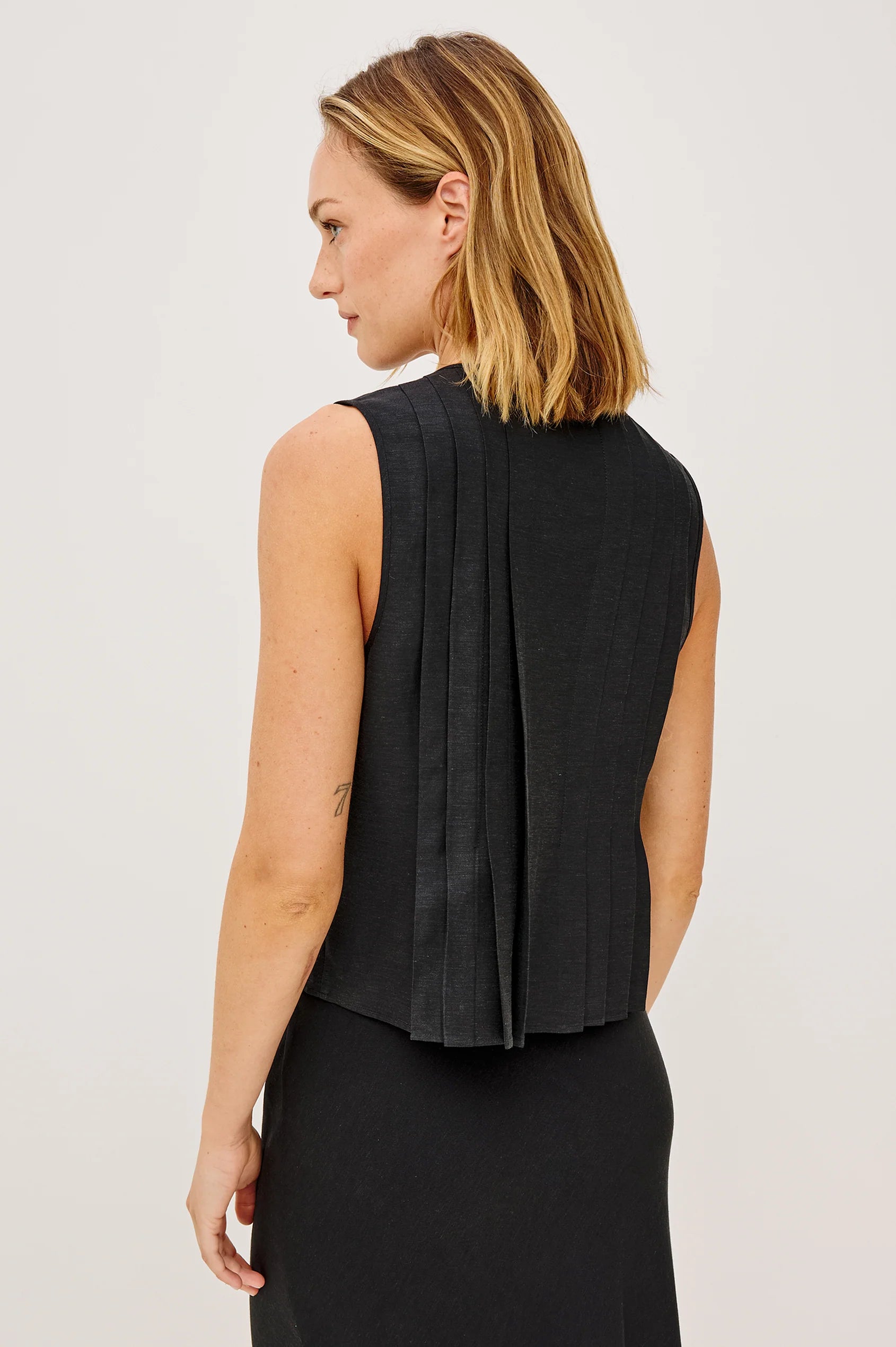 Woman wearing a black sleeveless top with a plain background