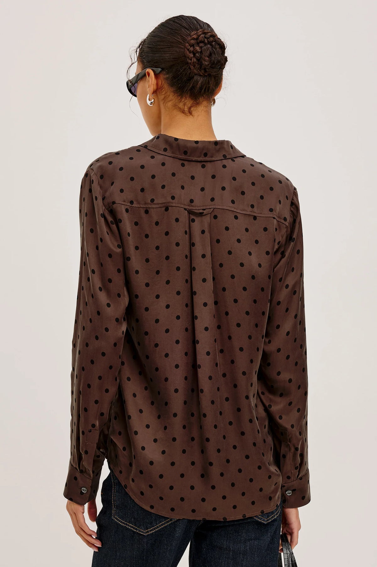 Person wearing a brown polka dot shirt on a plain background