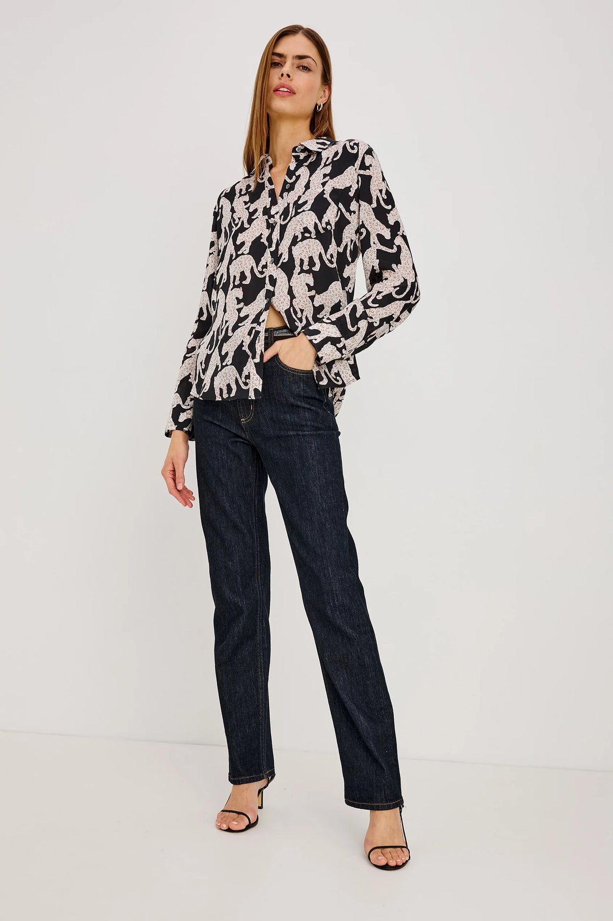 Woman wearing a patterned blouse and dark jeans on a white background
