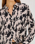 A woman wearing a black button-up shirt with an allover print of white and pink spotted leopards, paired with dark jeans.