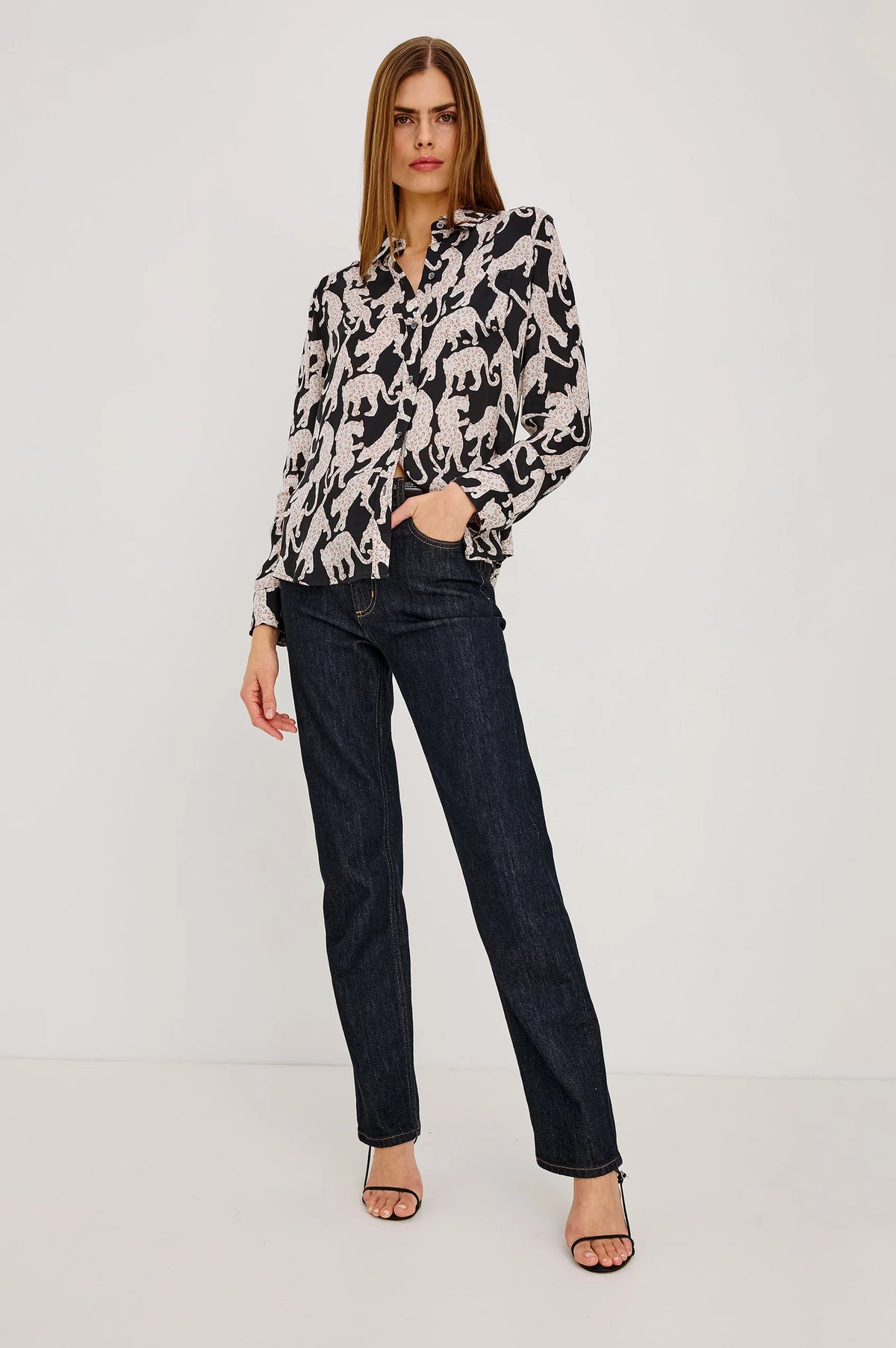 Woman wearing a patterned blouse and dark jeans on a white background