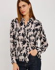 A woman modeling a black long-sleeve button-up blouse with an allover beige animal print, paired with dark blue jeans, against a plain light gray studio background.