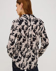 Woman wearing a black and white patterned blouse on a plain background