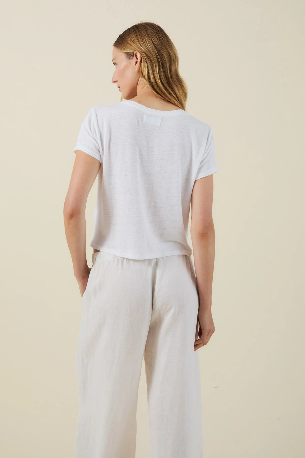 Woman wearing a white t-shirt and light-colored pants against a beige background