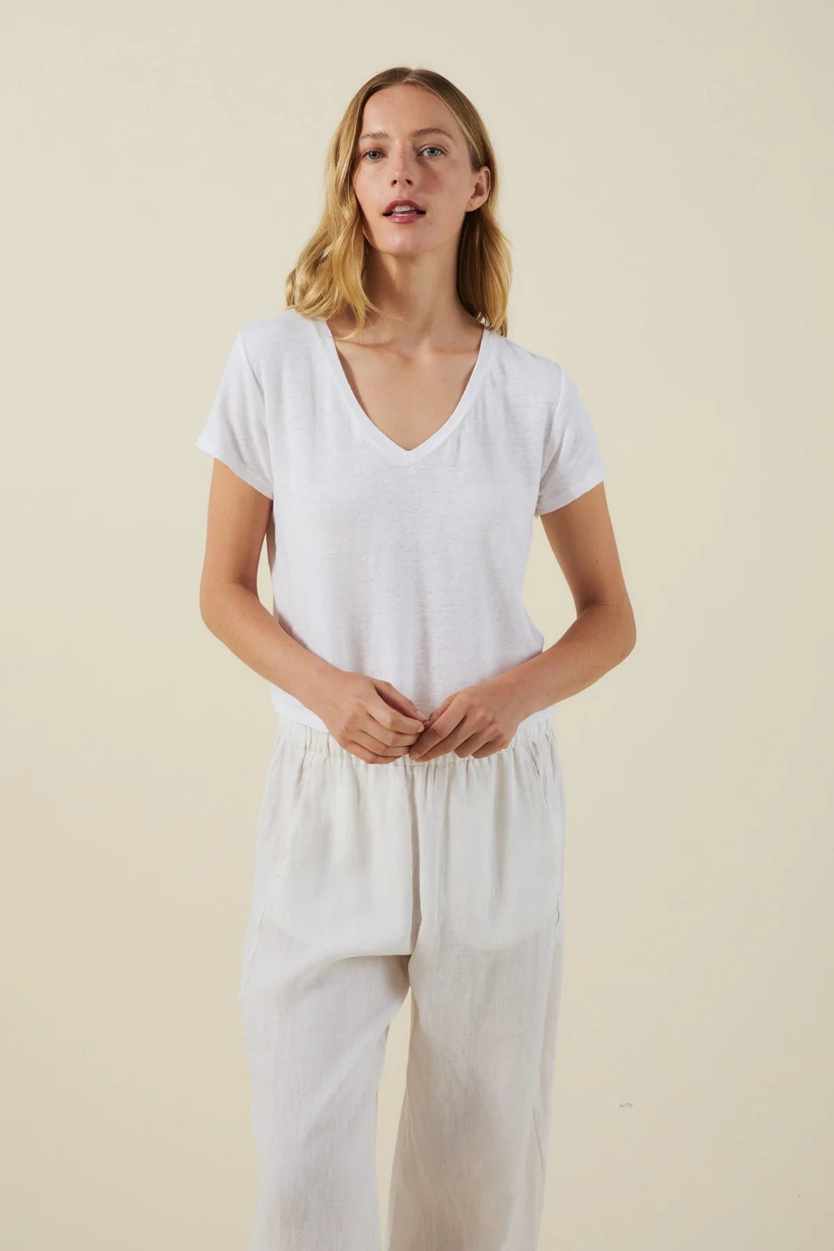 Woman wearing a white t-shirt and light-colored pants against a beige background
