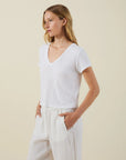 Woman wearing a white t-shirt and pants against a beige background