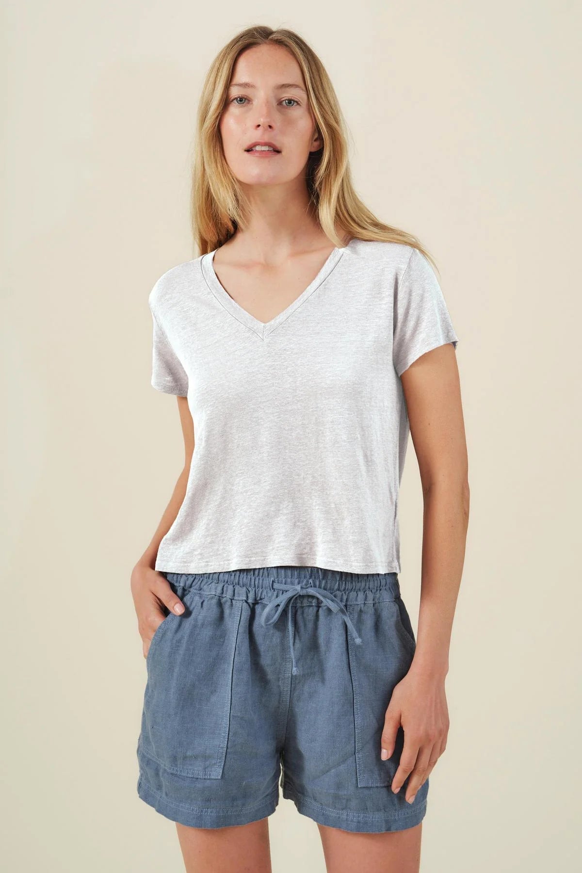 Woman wearing a white V-neck top and blue shorts on a beige background