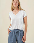 Woman wearing a white V-neck top and blue shorts on a beige background