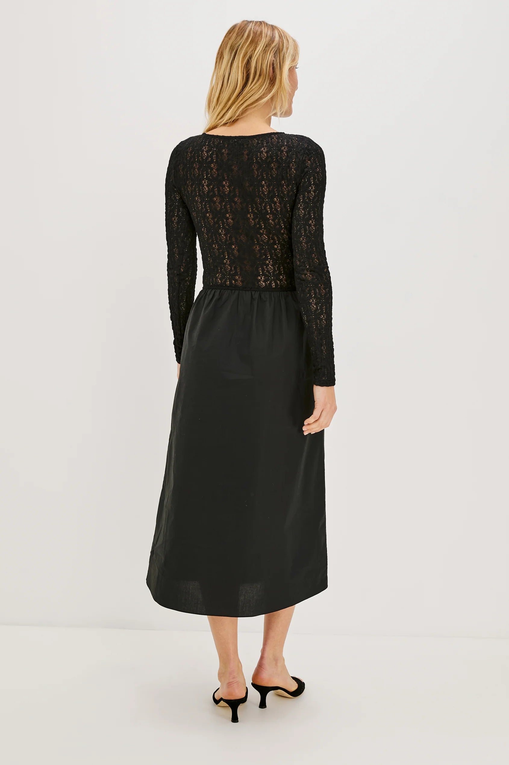 Woman wearing a black lace top and black skirt on a white background back view