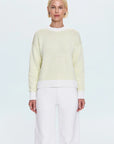 Person wearing a light yellow and white striped sweater with white pants on a plain background