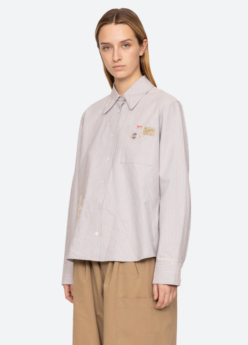 Person wearing a light gray shirt with embroidered patches on a white background