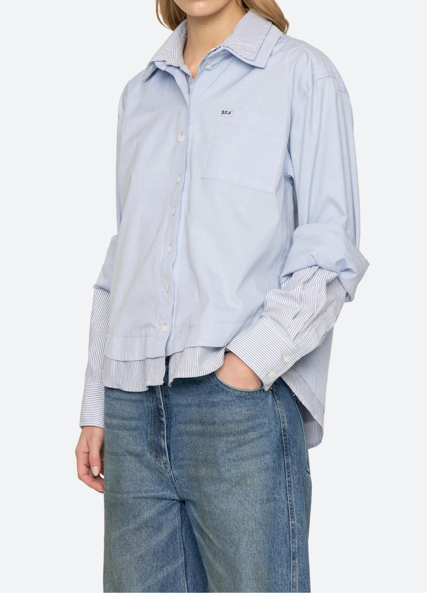 Woman wearing a light blue striped shirt and jeans on a white background, front/side view