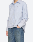 Woman wearing a light blue striped shirt and jeans on a white background, front/side view