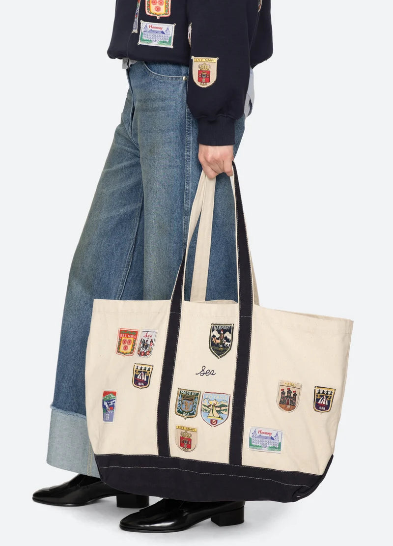 model holding a patchwork tote bag with jeans and boots on a white background