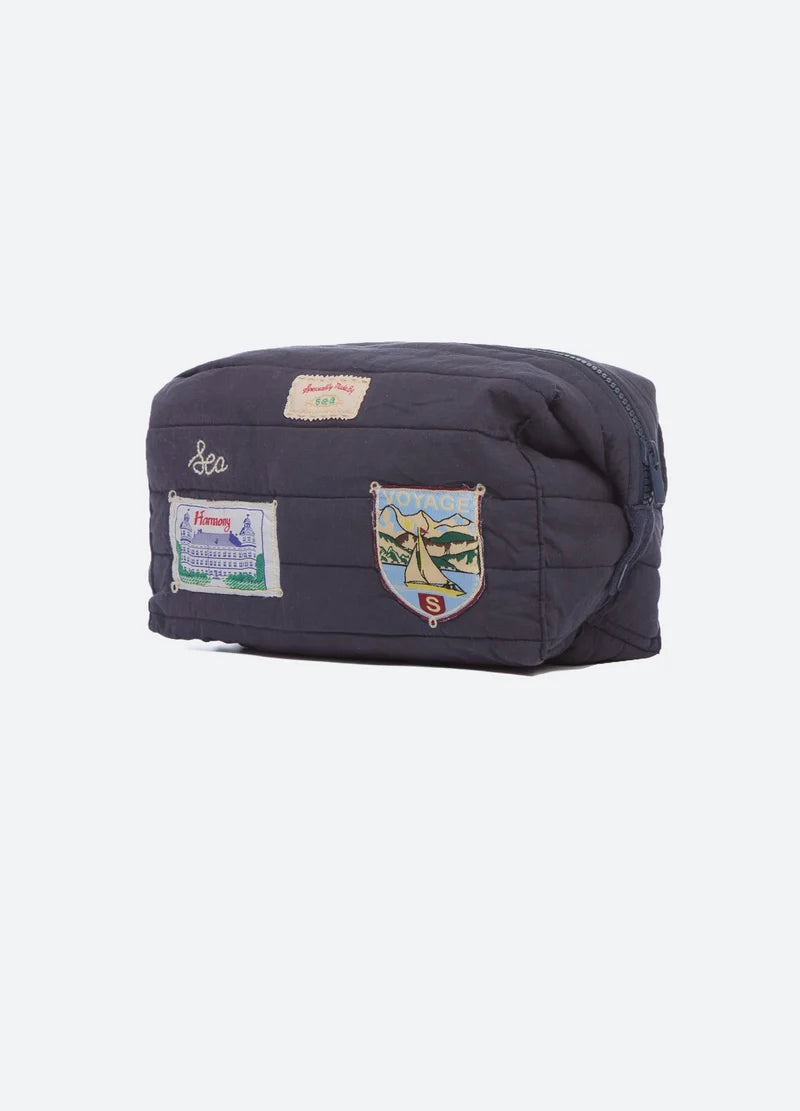 A dark navy blue quilted pouch bag with multiple embroidered patches and badges, shown against a plain light gray background.