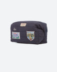 A dark navy blue quilted pouch bag with multiple embroidered patches and badges, shown against a plain light gray background.