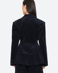 A model wearing a dark navy blue corduroy blazer paired with matching dark pants, against a light gray studio background, back view