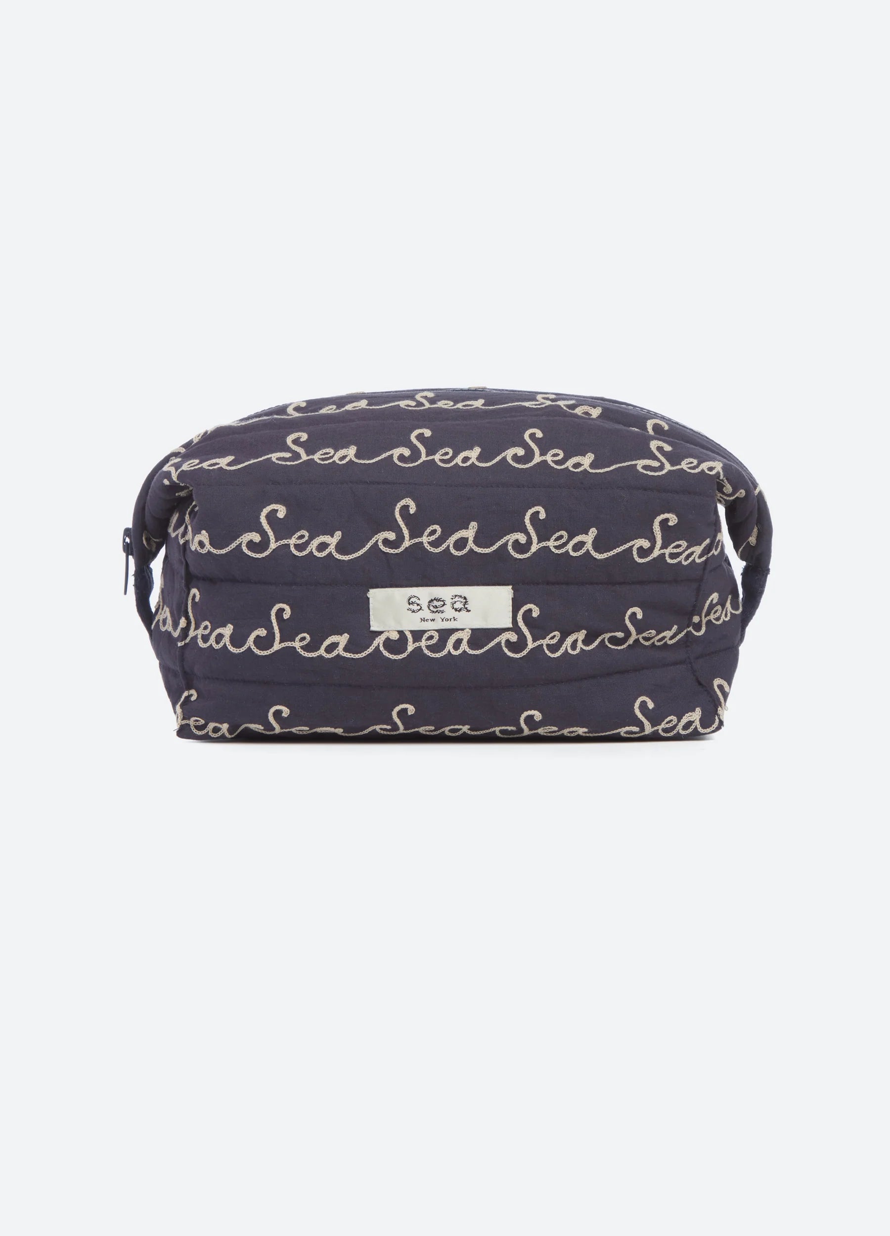 A navy blue quilted cosmetic pouch with an all-over beige script pattern reading 'Sea', featuring a small white brand label on the front.