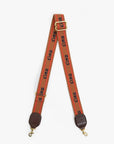 A wide orange-red fabric camera strap with a repeating black 'CIAO' logo print, featuring gold-tone metal hardware, a top adjustment buckle, and brown leather end caps with gold clasps, shown against a plain light gray background.